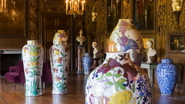 Large vases with colourful floral enamel decoration in Petworth's Carved Room against a backdrop of Grinling Gibbons wood carvings